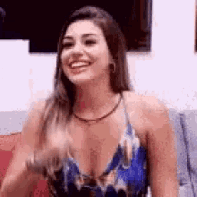 a woman is sitting on a couch smiling and waving her hand .