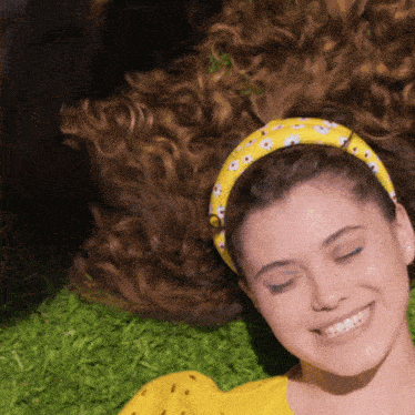 a woman wearing a yellow headband with white flowers is smiling