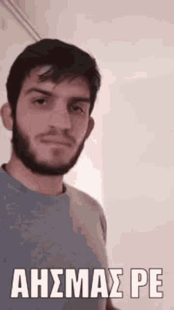 a man with a beard is wearing a gray shirt and has a foreign language written on his shirt .