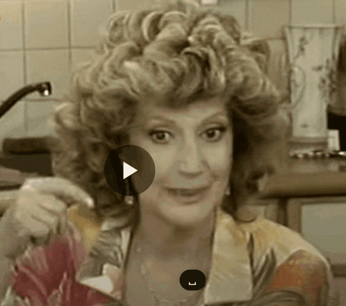 a woman with curly hair looks at the camera with a play button in front of her