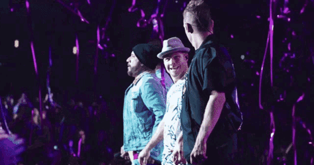 a group of men are standing on a stage with purple lights
