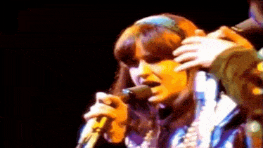 a woman is singing into a microphone while another person holds her head .