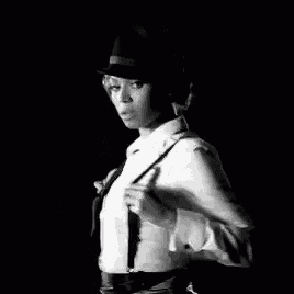 a black and white photo of a woman in a hat holding a whip .