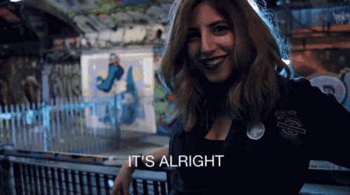 a woman smiles and says it 's alright in front of a graffiti wall