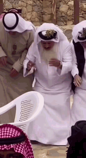 a man with a beard is sitting in a white chair with other men
