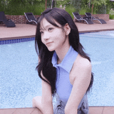 a woman in a blue shirt sits next to a swimming pool