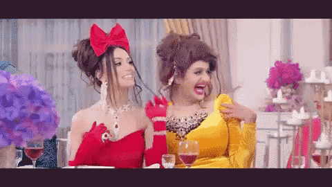 two women in red and yellow dresses are sitting at a table with glasses of wine .
