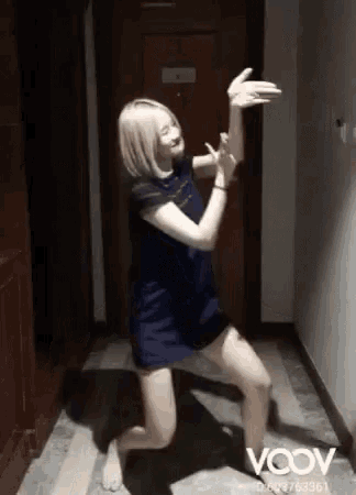 a woman in a blue dress is kneeling down in a hallway with her arms outstretched .
