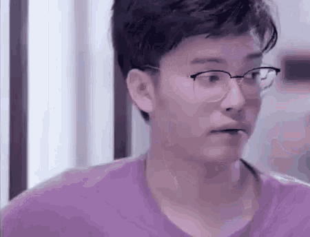 a man wearing glasses and a purple shirt is making a face .