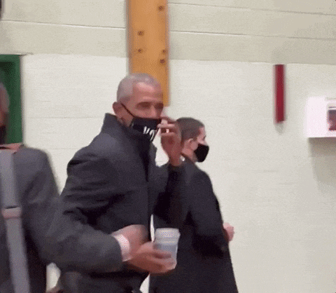 a man wearing a mask is holding a cup of water while walking .