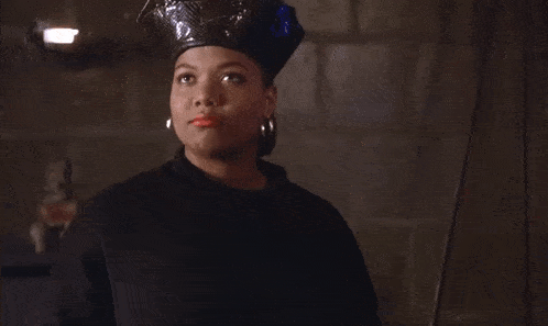 a woman wearing a black hat and earrings is standing in a dark room