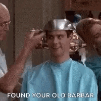 a man is getting his hair cut in a barber shop while wearing a metal helmet .