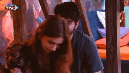 a man and a woman are hugging in front of a sign that says 24hr live channel .