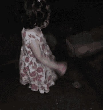 a little girl in a pink and white floral dress is standing in the dark .
