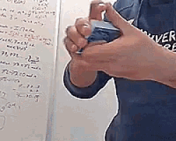 a person in a blue shirt is holding a cell phone in front of a white board with math problems on it .