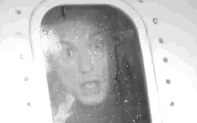 a black and white photo of a person looking out of a window .