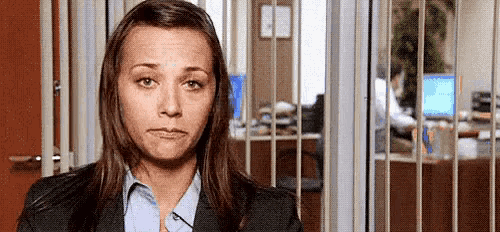 a woman in a suit and blue shirt is making a funny face in front of a window in an office .