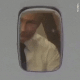 a man in a suit and tie is looking out of a window of an airplane .