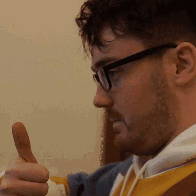 a man wearing glasses gives a thumbs up sign
