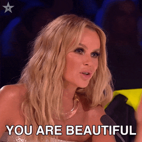 a blonde woman is sitting in front of a microphone with the words " you are beautiful " above her