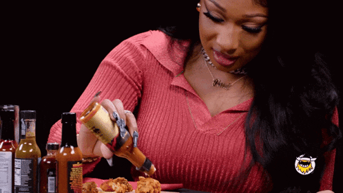 a woman in a red shirt is pouring hot sauce on a plate of food