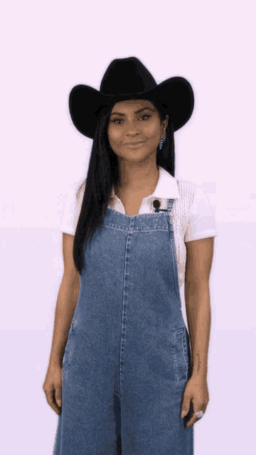 a woman wearing overalls and a cowboy hat smiles for the camera