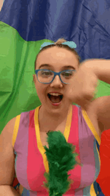 a woman wearing glasses and a colorful dress is giving a fist bump in front of a colorful flag .