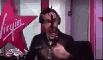 a man wearing headphones is standing in front of a microphone in a virgin radio studio .