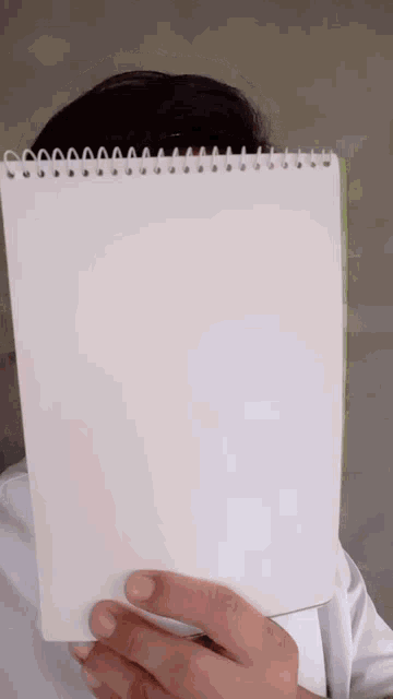a person covering their face with a spiral bound notebook