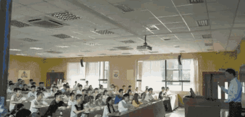 a large group of people are sitting in a lecture hall with a projector on the ceiling