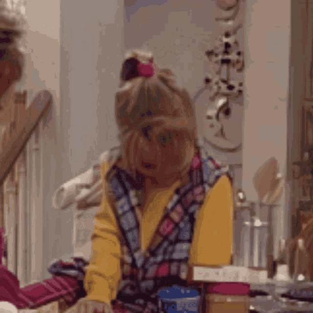 a girl in a plaid vest is sitting at a table in a kitchen
