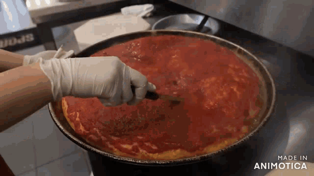 a person is spreading tomato sauce on a pizza in a pan that says made in animotica