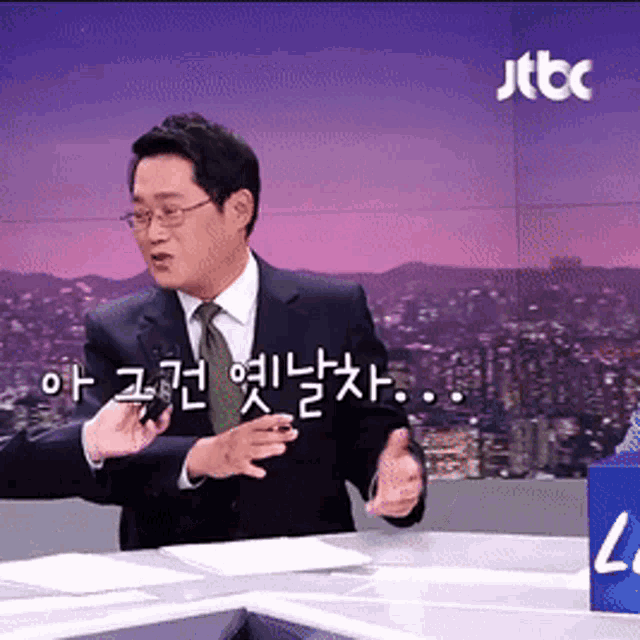 a man in a suit and tie is sitting at a desk with a sign that says jtbc