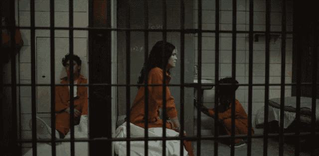 a man in an orange jumpsuit behind bars in a jail cell