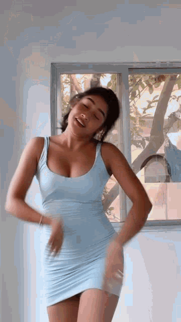 a woman in a light blue dress is dancing in a room in front of a window .