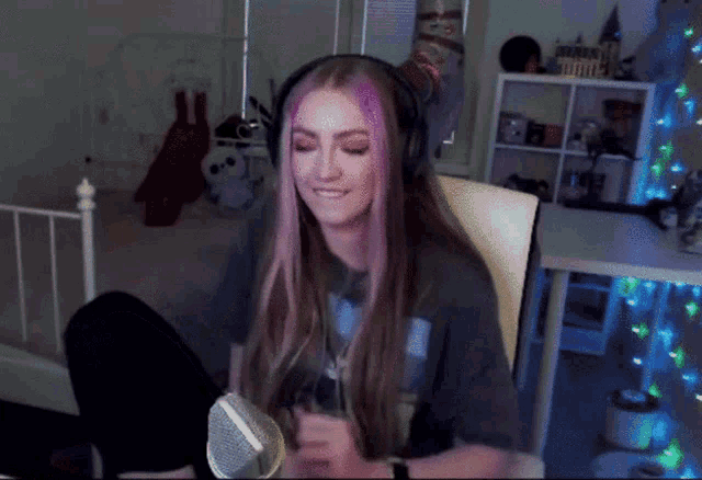 a girl with pink hair is sitting in front of a microphone and smiling