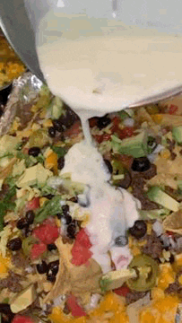 a close up of a person pouring ranch dressing on a nacho tray .