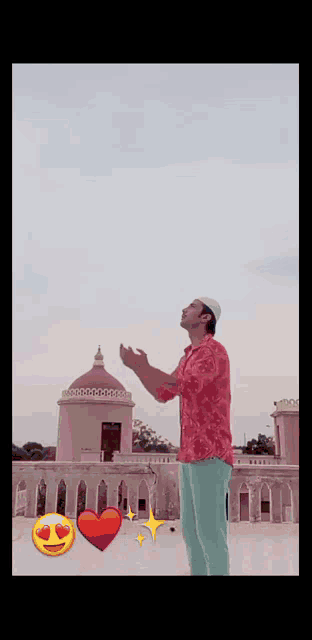 a man wearing a red shirt and a white hat is praying on a balcony