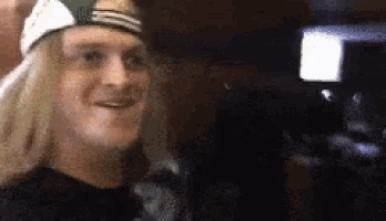 a man wearing a hat and a black shirt is smiling in a dark room .