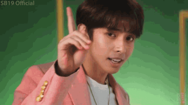 a young man in a pink jacket is pointing up with his finger