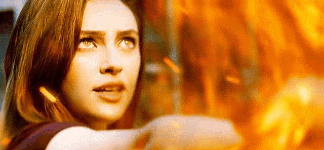a woman is standing in front of a fire looking up at it