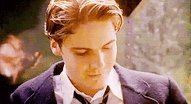 a young man in a suit and tie is looking down with his eyes closed .