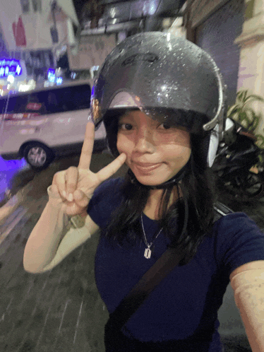 a woman wearing a motorcycle helmet giving a peace sign