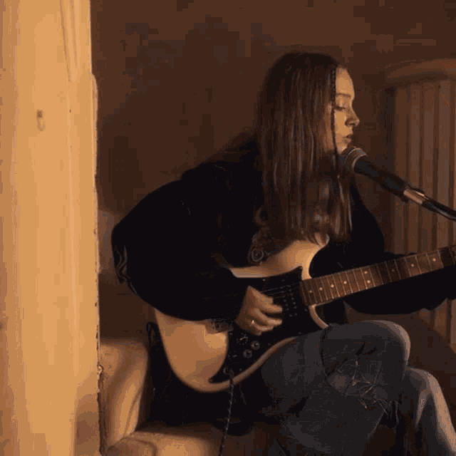 a woman playing a guitar and singing into a microphone
