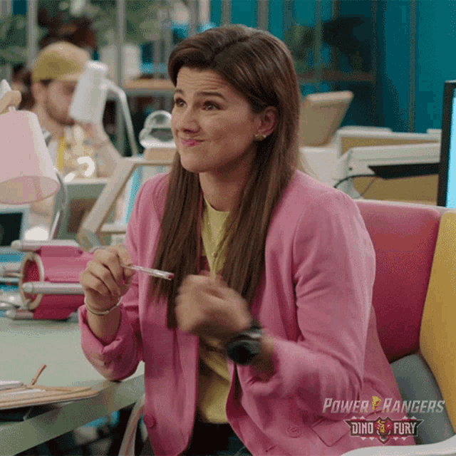 a woman wearing a pink power rangers jacket is sitting in an office