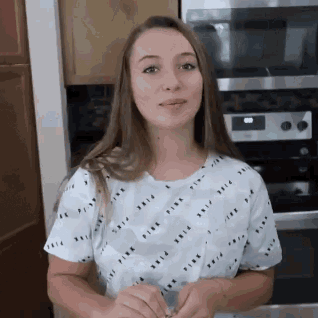 a woman wearing a pink shirt stands in front of a stove