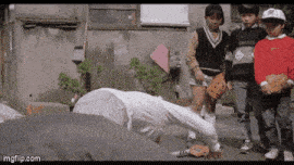 a group of children are standing around a man with his head on the ground ..