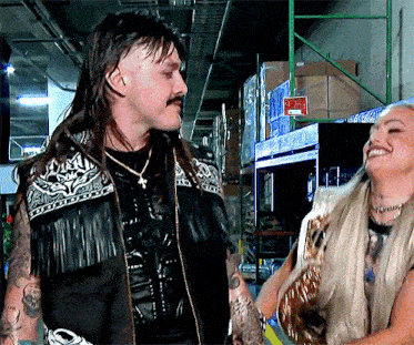 a man with a mullet and mustache is standing next to a woman in a warehouse