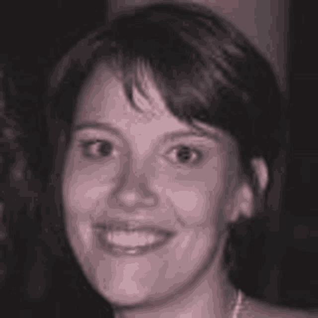 a woman is smiling in a black and white photo and looking at the camera .