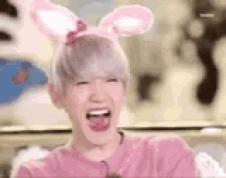 a boy wearing bunny ears and a pink shirt is laughing with his tongue out .